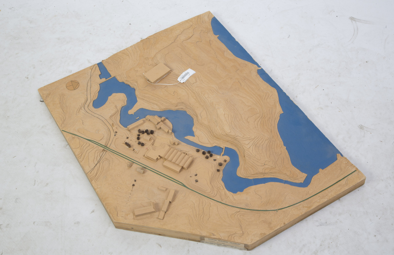 Arkitektmodell i papp som viser terreng, bygninger og elva i blått